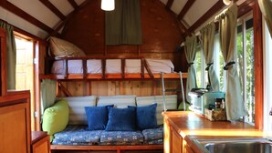 A cozy cabin interior with a bunk bed, a sofa with patterned cushions, a kitchen area with a sink, and a window with curtains.