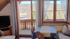 Ett rum med en balkong, en säng, en stol, ett bord och en tv.