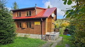 Une maison en bois avec un toit rouge, des fondations en pierre et un petit porche doté d’une rambarde en métal.