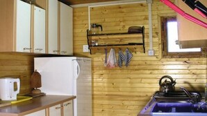 Une cuisine compacte aux murs en bois, avec un réfrigérateur blanc, un évier avec une bouilloire et une étagère contenant des ustensiles de cuisine.