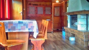 L’intérieur d’un chalet en bois comprend une table à manger, des chaises, une cheminée et une fenêtre avec des rideaux.