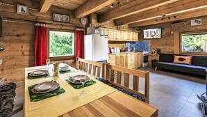 Interior de uma cabana de madeira com mesa de jantar posta, área de cozinha e um sofá.
