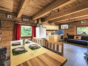 A wooden cabin interior with a dining table set, kitchen area, and a sofa.