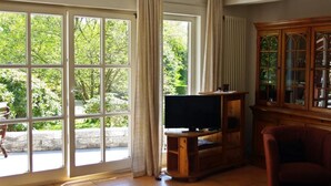A living room with a large sliding glass door, a television on a wooden stand, and a red armchair. - Göttert by Interhome (Dickenschied)