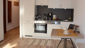 Une cuisine compacte avec des meubles blancs, un four encastré, une machine à café et une table à manger avec un set de table.