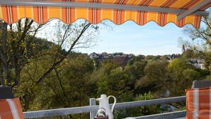 Une terrasse avec une table dressée pour le petit-déjeuner, offrant une vue panoramique sur les arbres et les maisons.