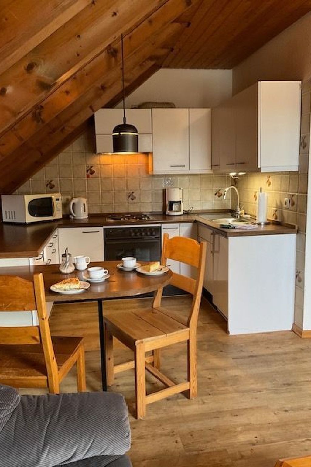 Une cuisine chaleureuse avec des poutres en bois, une table à manger avec des chaises et un petit îlot central doté d’un évier.