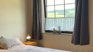 Quarto com uma cama grande, mesa de cabeceira com luminária, janela com cortinas e vista para o exterior.