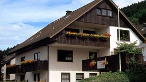 Um edifício de dois andares com telhado inclinado, varandas com caixas de flores e uma placa indicando um restaurante.