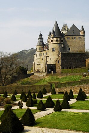 Eine Burg mit mehreren Türmen und einem gepflegten Garten mit ordentlich geschnittenen Hecken.