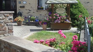 A building with a brick facade, a wooden pergola with a sign, and flower beds with pink flowers. - Elztalblick by Interhome (Bereborn)