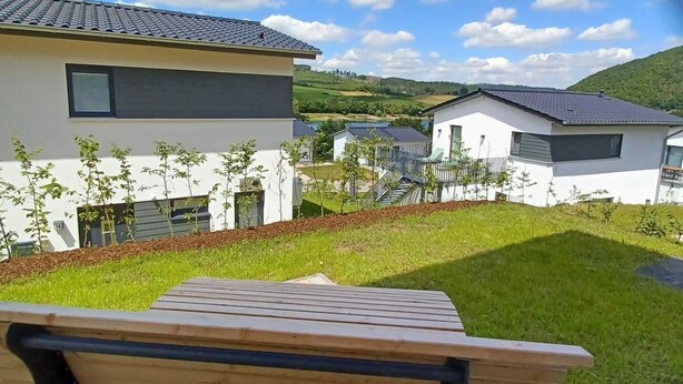Un espace extérieur moderne aménagé avec un banc, une terrasse pavée et une vue sur des immeubles résidentiels et un paysage vallonné.