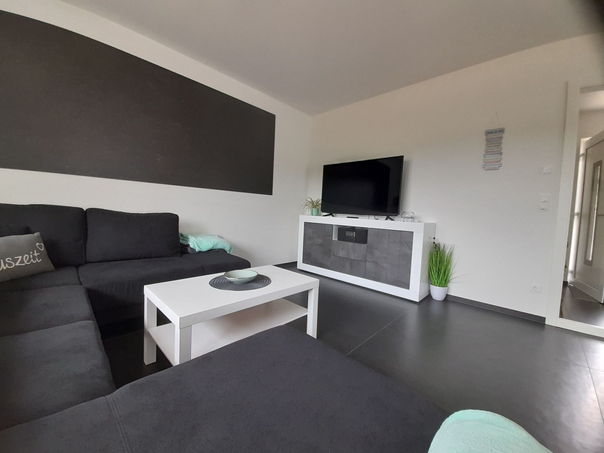 Un salon moderne avec un canapé de couleur foncée, une table basse blanche et un téléviseur à écran plat fixé à un meuble blanc.