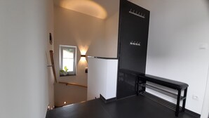 Un intérieur moderne avec un escalier, un banc, une lampe fixée au mur et une fenêtre agrémentée d’une plante.