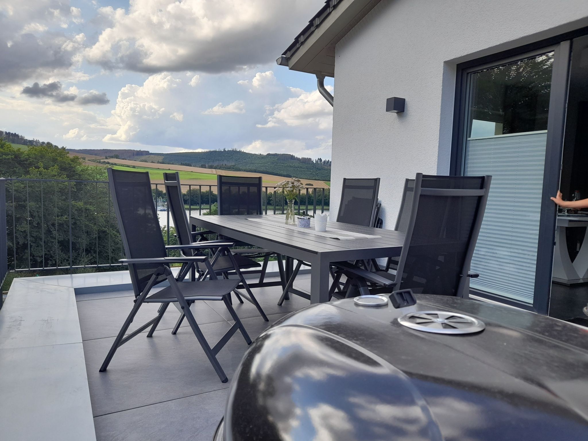Una terrazza esterna con tavolo e sedie, un barbecue e vista sulla campagna.