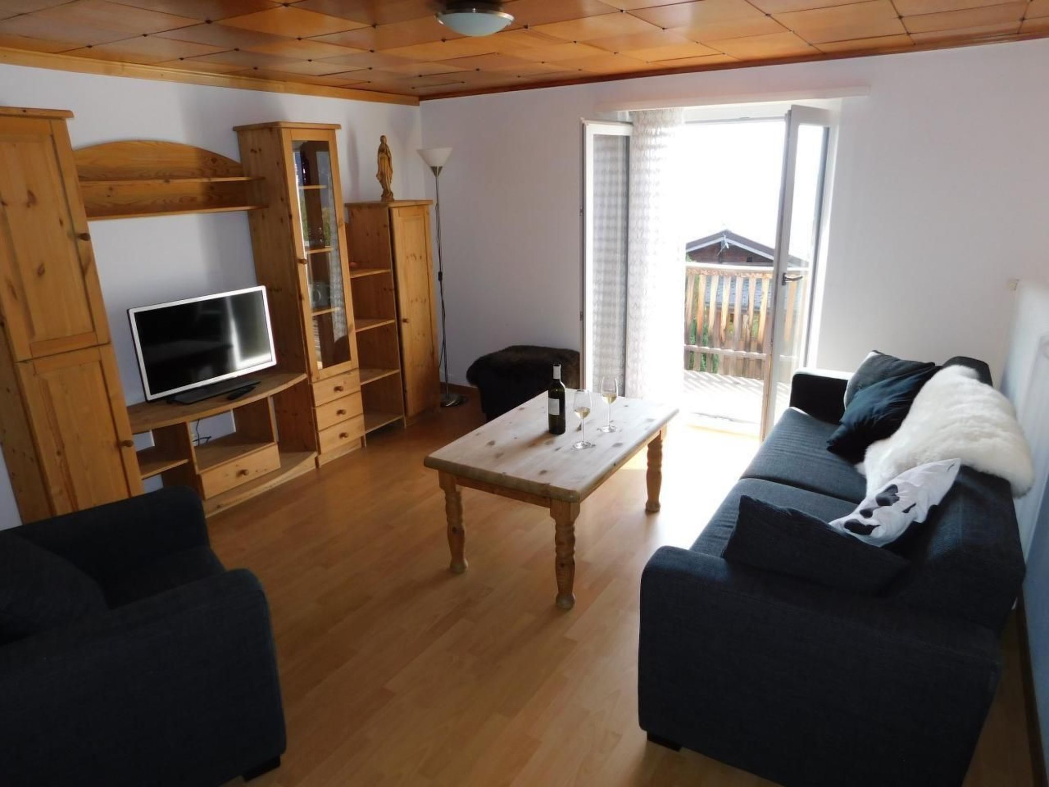 Ein Wohnzimmer mit Fernseher, Holzmöbeln, einem Tisch mit Weingläsern und einer Couch.