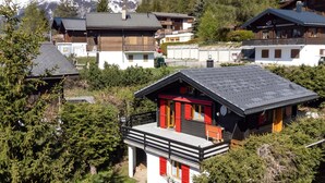 Un bâtiment de style chalet, doté d’un balcon, entouré d’arbres et avec des montagnes enneigées en arrière-plan.