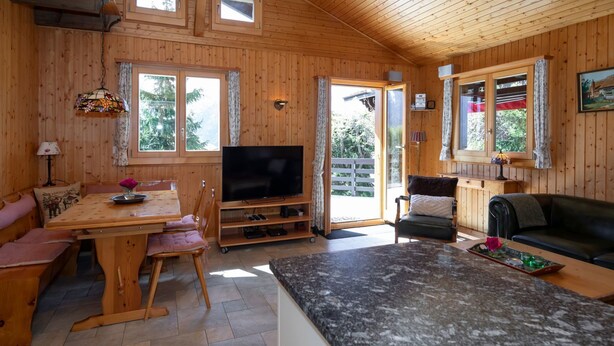 L’intérieur d’un chalet en bois chaleureux et accueillant, comprenant un coin repas, un salon et un téléviseur.