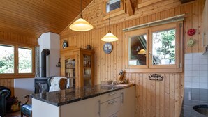 Une cuisine rustique, aménagée dans une cabane en bois, avec un îlot central, des luminaires suspendus et une cuisinière encastrée.
