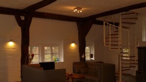 A spacious living room with a high ceiling, exposed wooden beams, a built-in sofa, a coffee table, and a spiral staircase. - Haus Siedschelje by Interhome (Schwanewede)