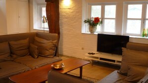 A living room with a sofa, a coffee table, a TV, and a window with a vase of flowers. - Haus Siedschelje by Interhome (Schwanewede)