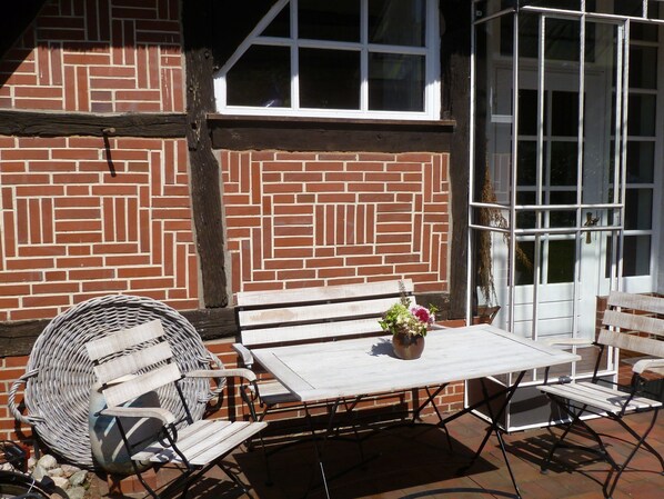 An outdoor patio with a brick wall, a white table, and wicker chairs.