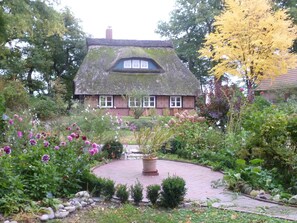 A traditional house with a thatched roof, surrounded by a well-maintained garden with various flowers and shrubs.