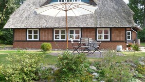 A thatched-roof house with a dining area and a large umbrella. - Haus Siedschelje by Interhome (Schwanewede)