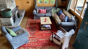 Ein gemütliches Wohnzimmer mit Kamin aus Stein, einem grauen Sofa, einem gemusterten Teppich und einem Holztisch.