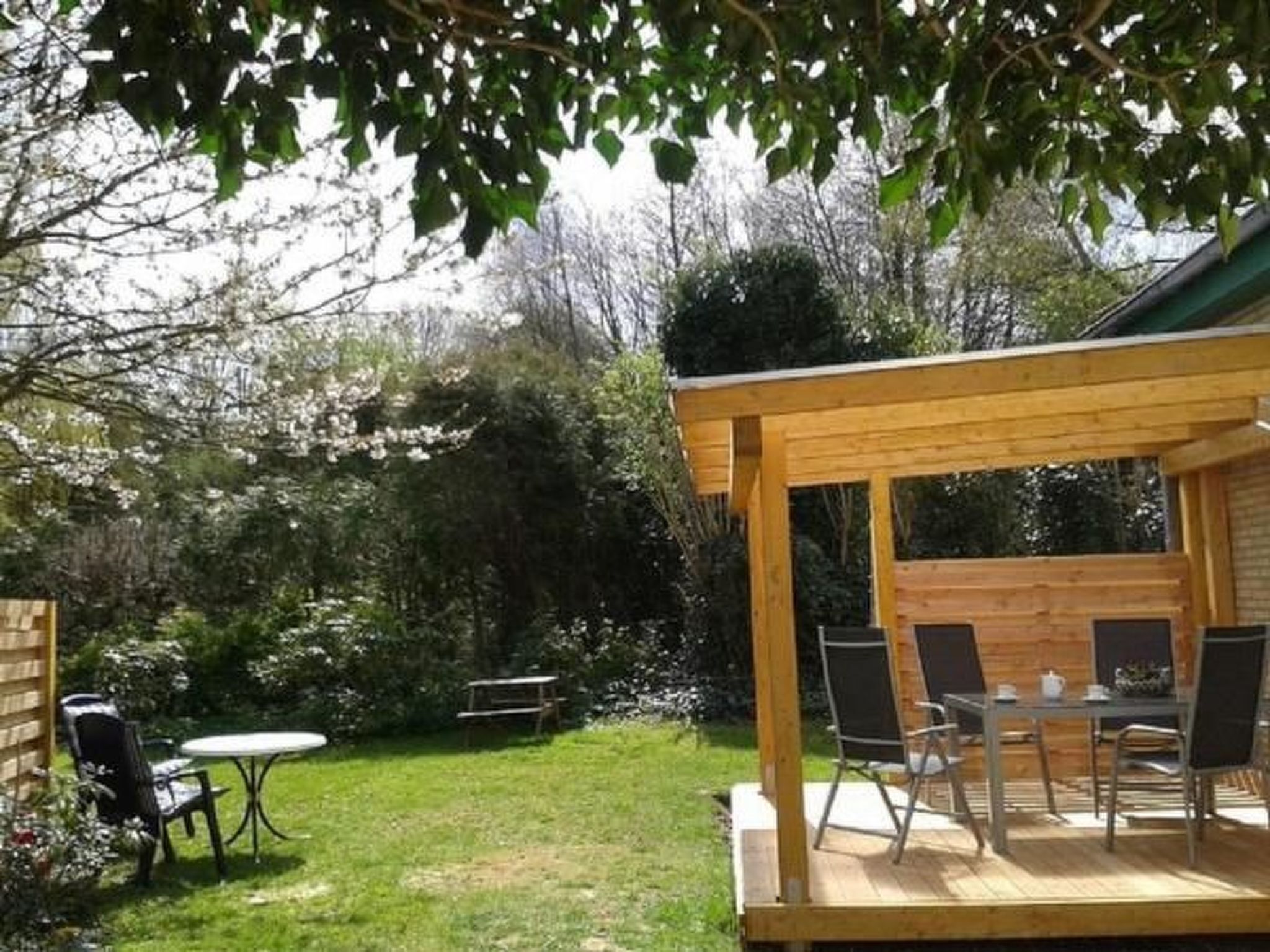 A wooden pergola with a table and chairs in a garden setting.