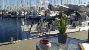 A marina with multiple sailboats docked. There is a covered area with a table and chairs, and a potted plant on the deck. - Apartment Ole by Interhome (Oldenburg in Holstein)
