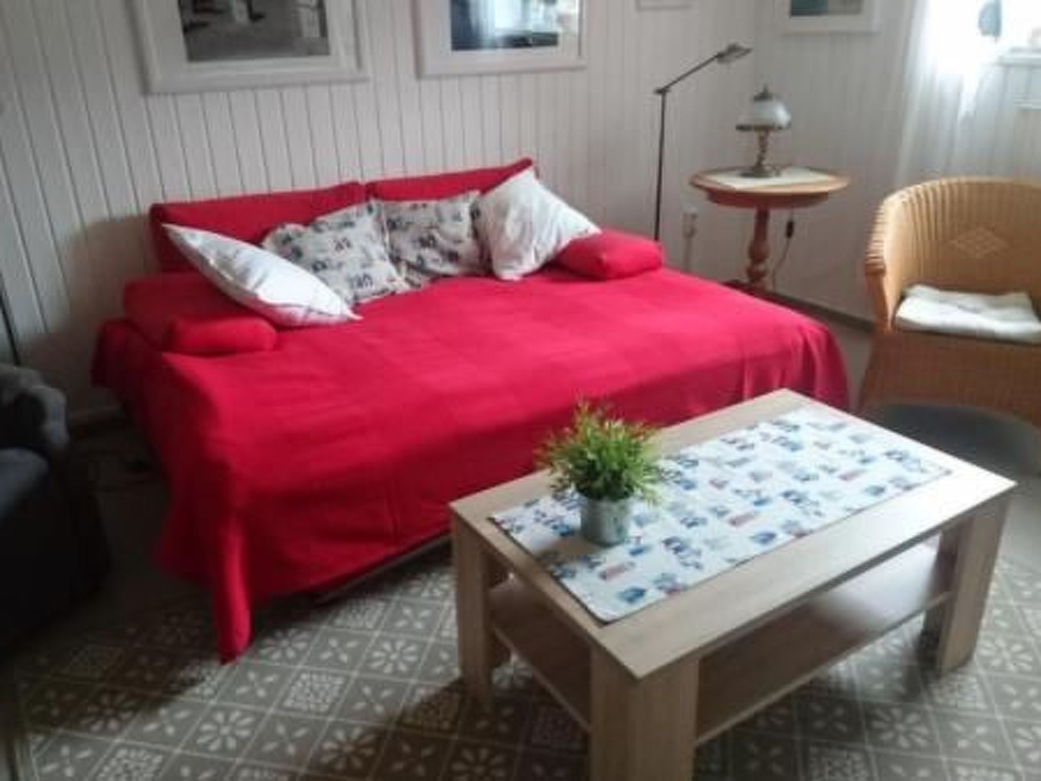 Una habitación con un sofá rojo, una mesita con una planta y baldosas de suelo estampadas.