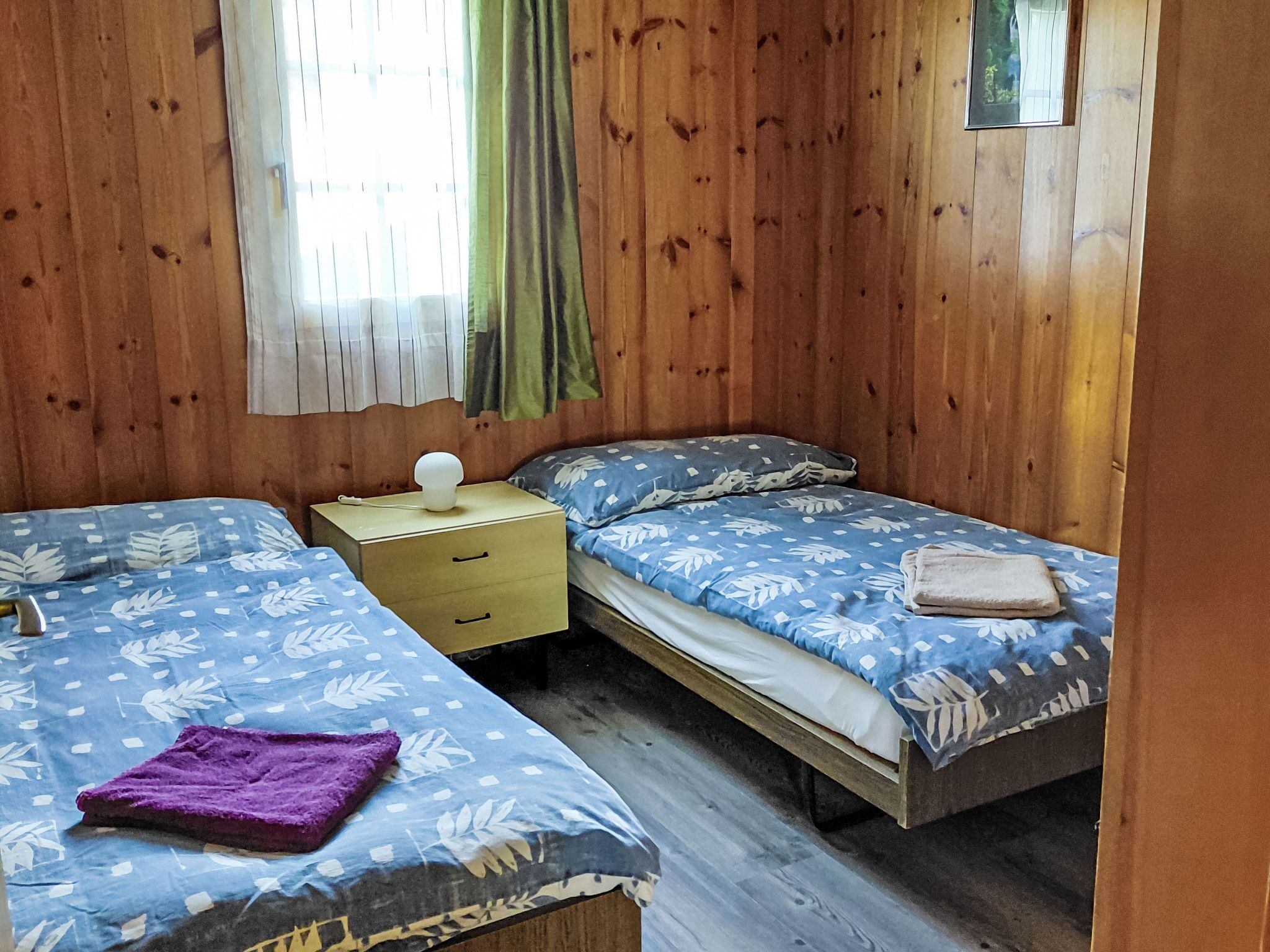 Quarto com duas camas, uma mesa de cabeceira e janela com cortinas.