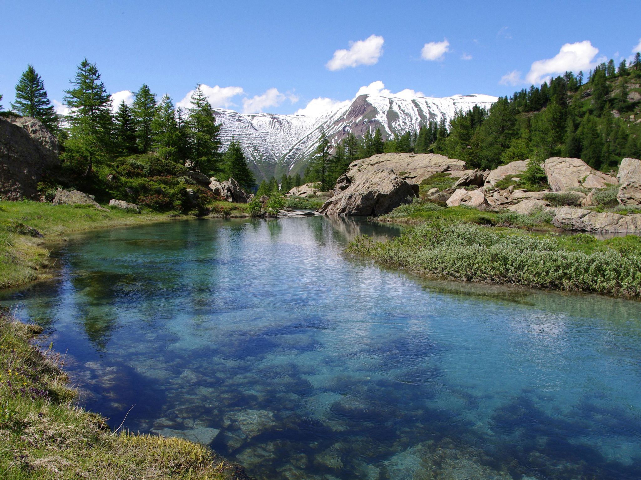 Un lago alpino limpido circondato da rocce e alberi.