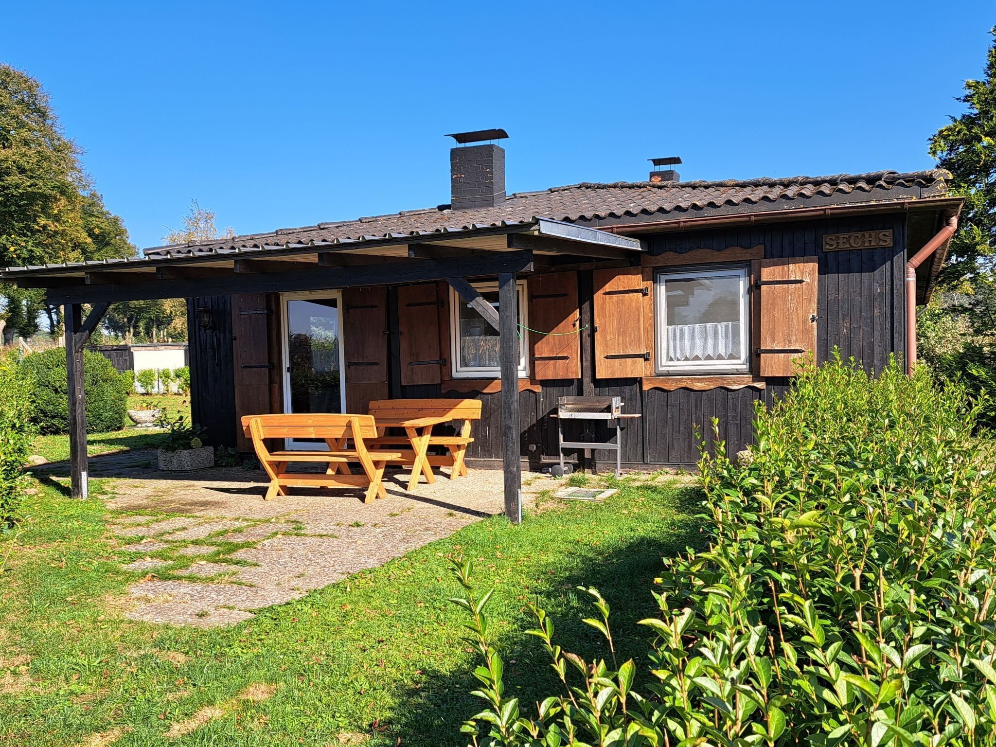 Uma cabana de madeira com varanda, uma mesa e bancos.