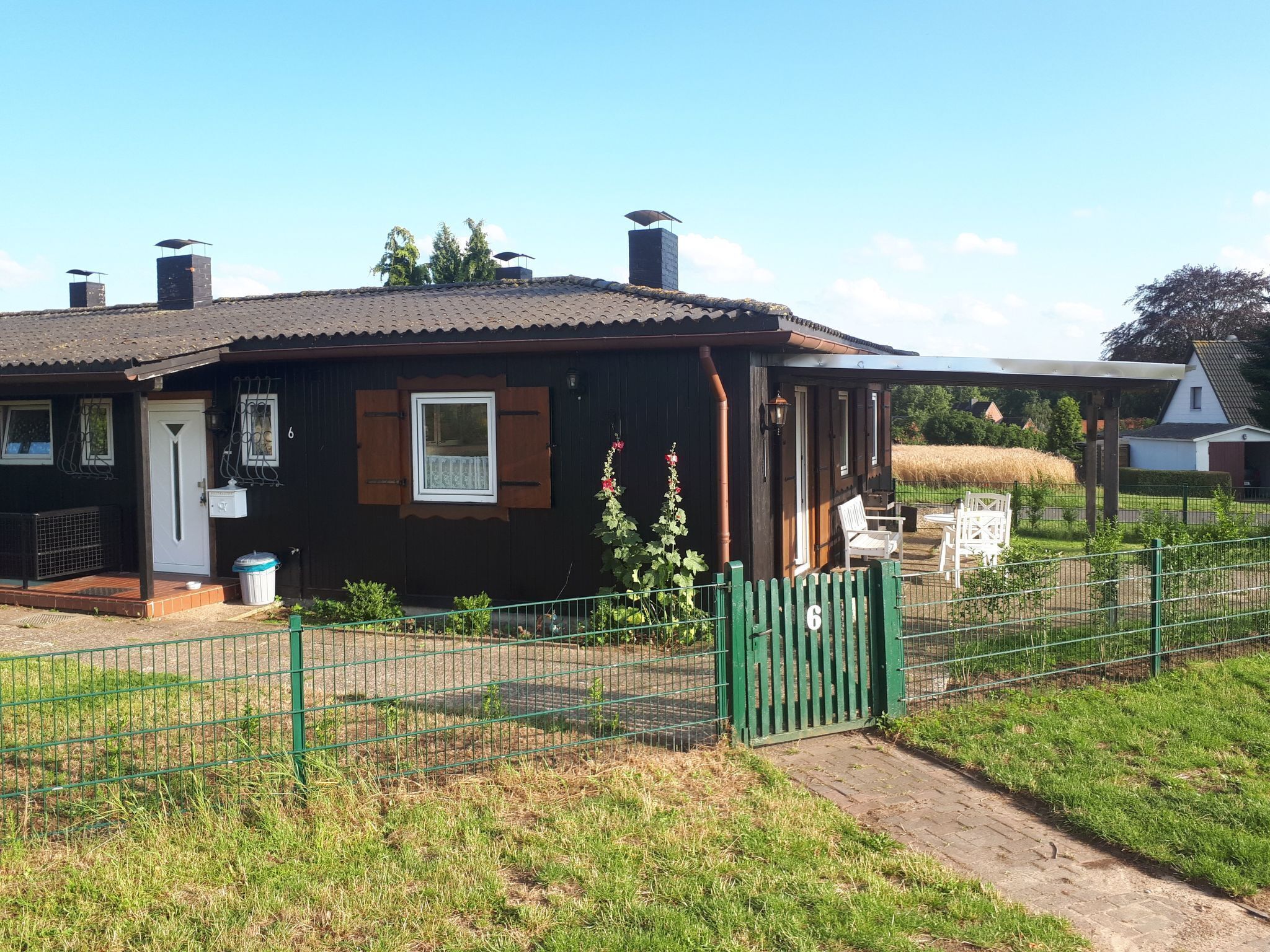 Une maison de campagne en bois, avec un toit en tuiles, un petit porche et un jardin clos.