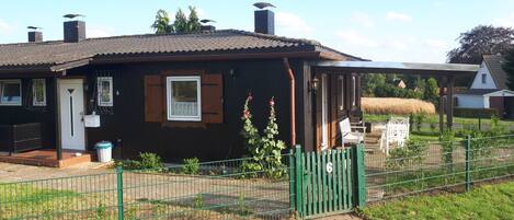 Une maison de campagne en bois, avec un toit en tuiles, un petit porche et un jardin clos.