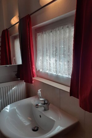 Ein Badezimmer mit einem weißen Waschbecken, einem Spiegel und einem Fenster mit Spitzenvorhängen.
