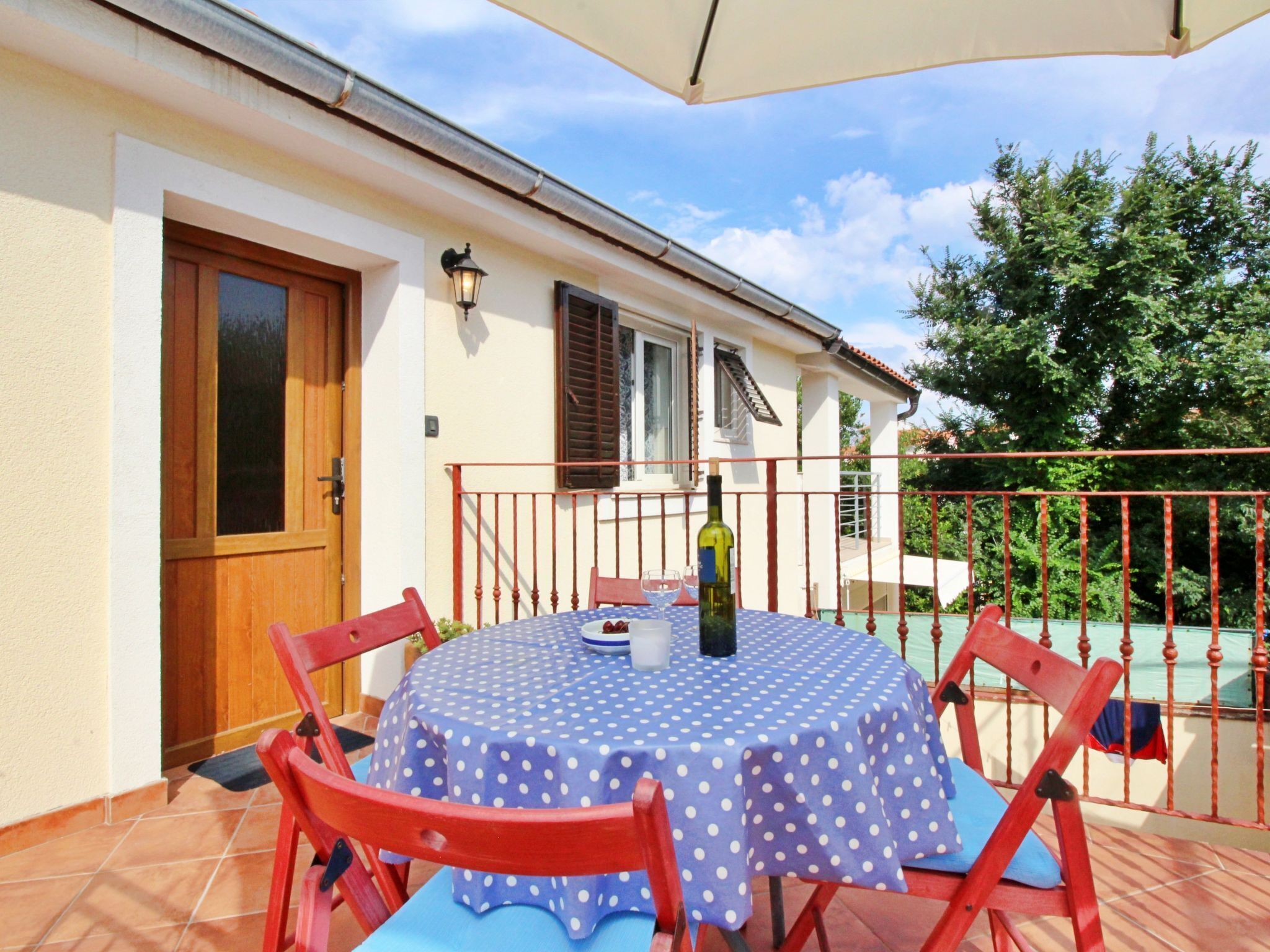 Eine Terrasse mit einem runden Tisch, bedeckt mit einer Tischdecke mit Punkten, umgeben von roten Stühlen.