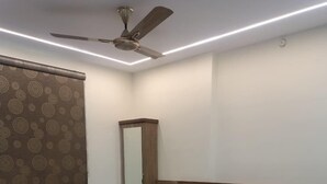 Ein Schlafzimmer mit Bett, Deckenventilator, Spiegel und Fenster mit gemustertem Vorhang.