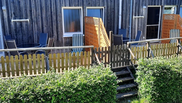 A wooden building with a wooden fence, a small staircase, and a garden area with bushes. - Fewo "Edison" by Interhome (Holzdorf)