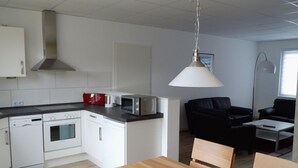 A modern kitchen with white cabinets, a microwave, and a coffee maker. There is a dining table with chairs in the foreground. - Fewo "Edison" by Interhome (Holzdorf)