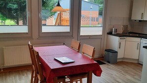 A dining area with a red table and chairs, a book on the table, and a view of the outside through large windows. - Fewo "Edison" by Interhome (Holzdorf)