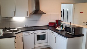 A compact kitchen with white cabinets, a dishwasher, an oven, a microwave, and a coffee maker. - Fewo "Edison" by Interhome (Holzdorf)