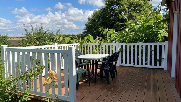Una terraza de madera con cercado blanco, una mesa y sillas.