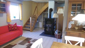 Un salón acogedor con un sofá rojo, una mesa de madera, una silla blanca, una escalera y una chimenea.