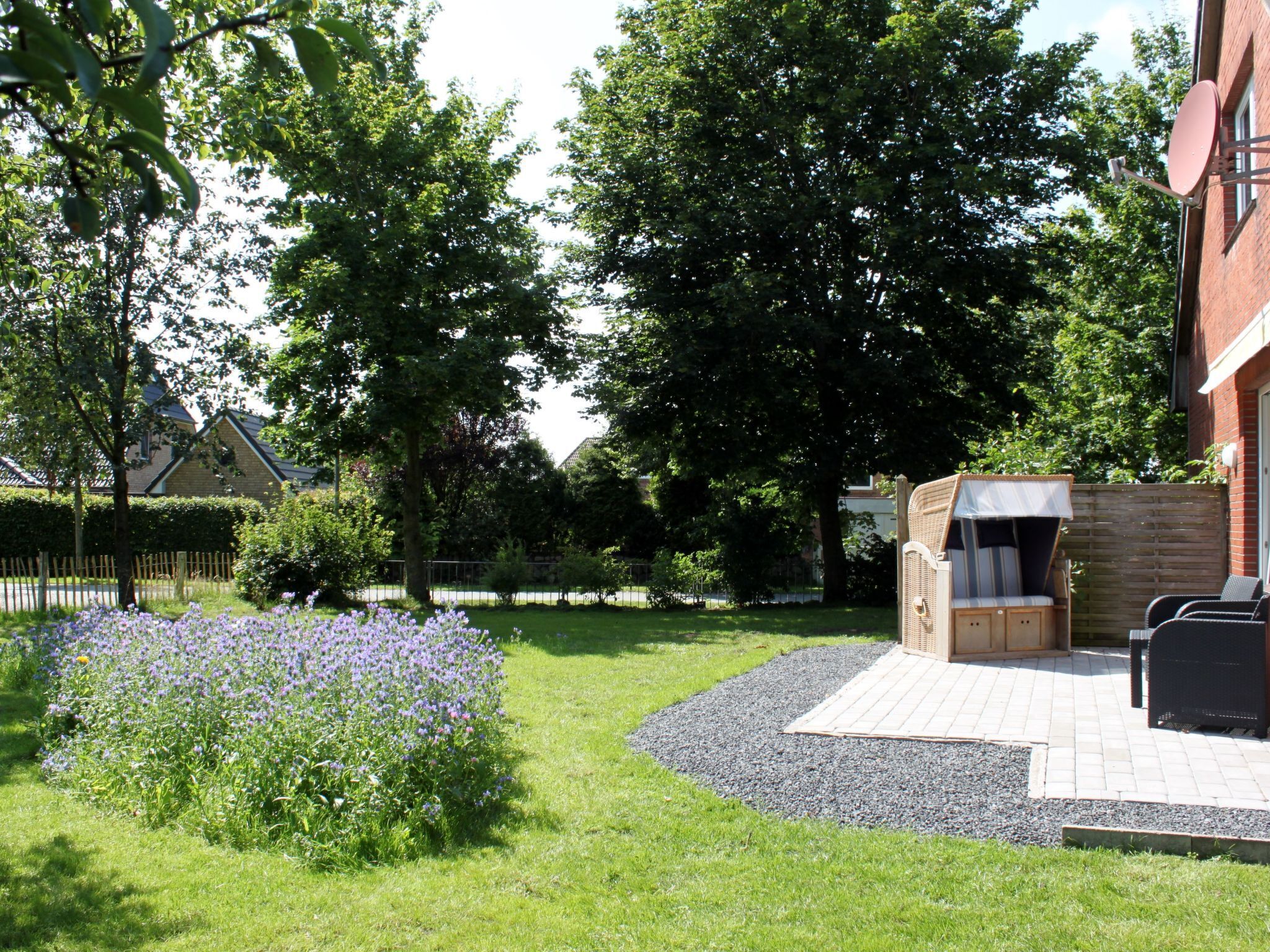 Eine Terrasse mit Grill, Sitzgelegenheit und einem Garten mit violetten Blumen.
