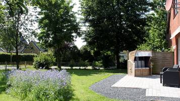 Eine Terrasse mit Grill, Sitzgelegenheit und einem Garten mit violetten Blumen.