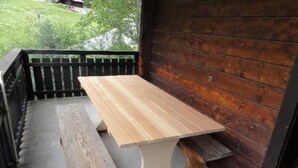 Een houten tafel met bankjes op een veranda, voorzien van een houten leuning en uitzicht op een groen landschap.