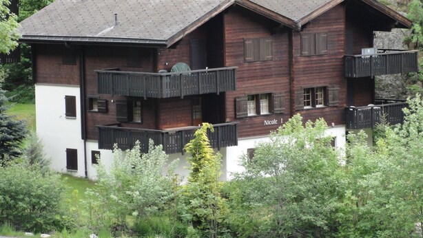 Een houten chalet met meerdere verdiepingen en balkons, omgeven door weelderige begroeiing.